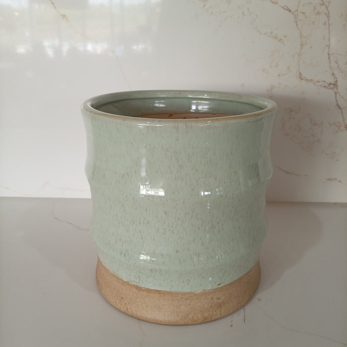 Fluted celadon green glazed ceramic planter vase with a glossy speckled upper body and a raw unglazed earthy base.