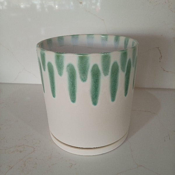 A cylindrical white ceramic planter pot featuring a decorative green drip glaze pattern along the upper rim, sitting on a matching white saucer.