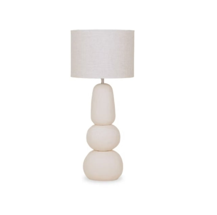 Contemporary cream-coloured ceramic table lamp with an elongated, stacked three-tier stone silhouette base and a matching linen drum shade.