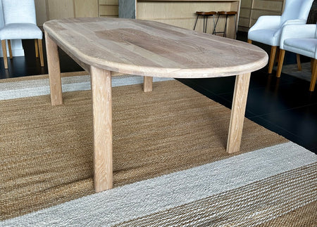 Clean, empty profile shot of the handcrafted 2200mm solid oak oval dining table sitting on a striped natural fiber rug.