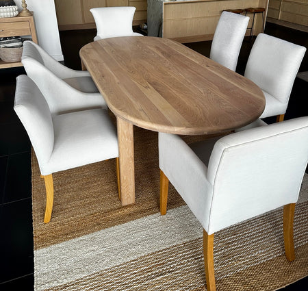 Handcrafted solid oak oval dining table styled for context with upholstered linen chairs (chairs sold separately).