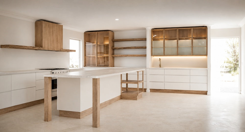 Bespoke modern open-plan kitchen design featuring seamless white handleless cabinetry, a large kitchen island with raw timber legs, and luxury glass-front display cabinets by Urban Yuppi.